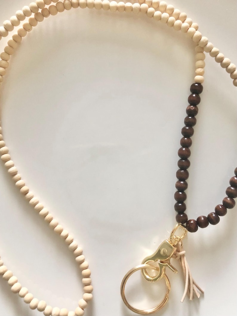 May include: A brown and natural wood beaded lanyard with a gold metal key ring and a brown tassel.