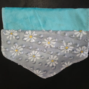 May include: A gray and white fabric with a daisy pattern and a light blue fabric on top. The fabric is folded in half and has a triangular shape.