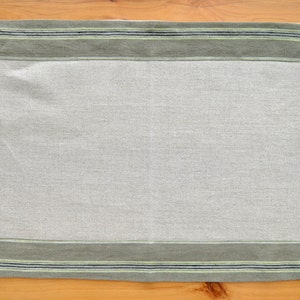 May include: A light gray linen placemat with a green and black striped border.