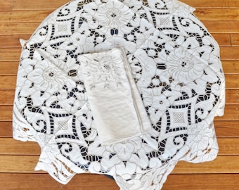 Puede incluir: Mantel de encaje blanco con un delicado patrón floral. El mantel está doblado por la mitad y colocado sobre una superficie de madera.