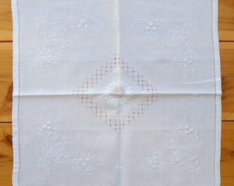 Puede incluir: Mantel de lino blanco con delicados diseños florales bordados y un patrón central en forma de diamante.