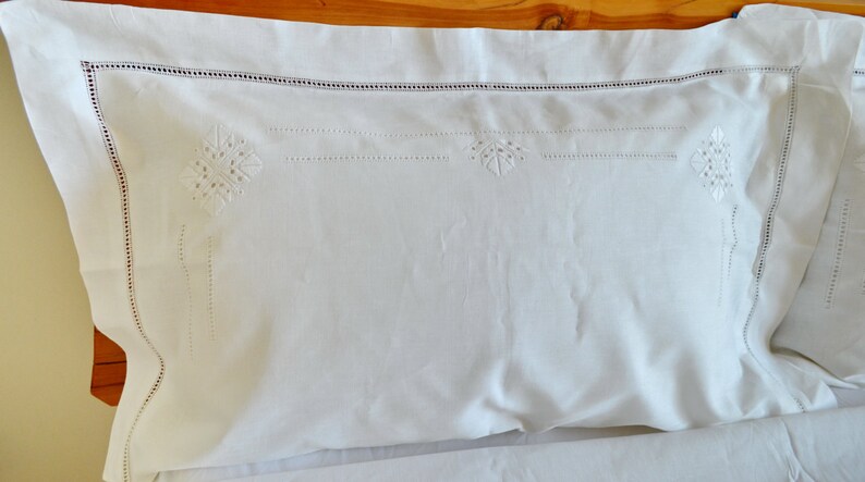 May include: White pillowcase with delicate embroidered floral designs. The pillowcase has a white border with a subtle scalloped edge.
