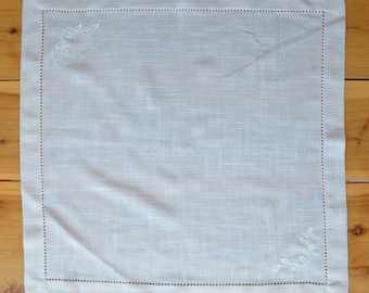 May include: A white linen napkin with a delicate embroidered design of leaves in each corner.