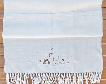 May include: White linen table runner with a delicate floral embroidery design and a fringe border.