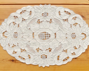 May include: White oval lace tablecloth with a delicate floral design. The lace is intricate and features a repeating pattern of flowers and leaves.