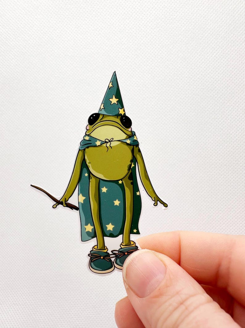 Pu&ograve; includere: Una rana verde che indossa un cappello da mago e un mantello con stelle blu e gialle, tenendo un bastone. La rana indossa scarpe blu con lacci gialli.