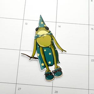 Frog wearing star covered cape and wizard hat.