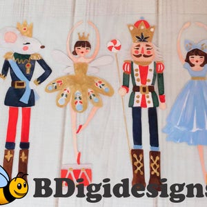 May include: Four paper cutouts of characters from a Nutcracker ballet: a mouse king, a ballerina, a nutcracker soldier, and a ballerina in a blue dress. The characters are on a white wood background.