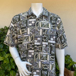 May include: Short-sleeved button-down shirt with a repeating pattern of green, black, and tan squares. The shirt is displayed on a mannequin. The pattern includes stylized leaf and geometric designs. The shirt has a collared neckline and wooden buttons.