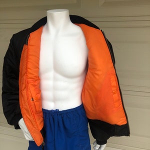 May include: A black bomber jacket with an orange lining. The jacket is unzipped and the lining is visible. The jacket is on a white mannequin.