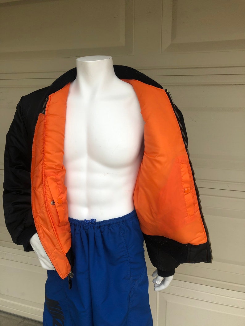 May include: A black bomber jacket with an orange lining. The jacket is unzipped and the lining is visible. The jacket is on a white mannequin.