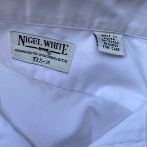 May include: White dress shirt with a label that reads "Nigel White" and "55% Polyester-35% Combed Cotton" and "17 1/2 - 35". The label also has a small bow tie graphic. A second label reads "Made in Korea RN 67552 Reverse for Care".