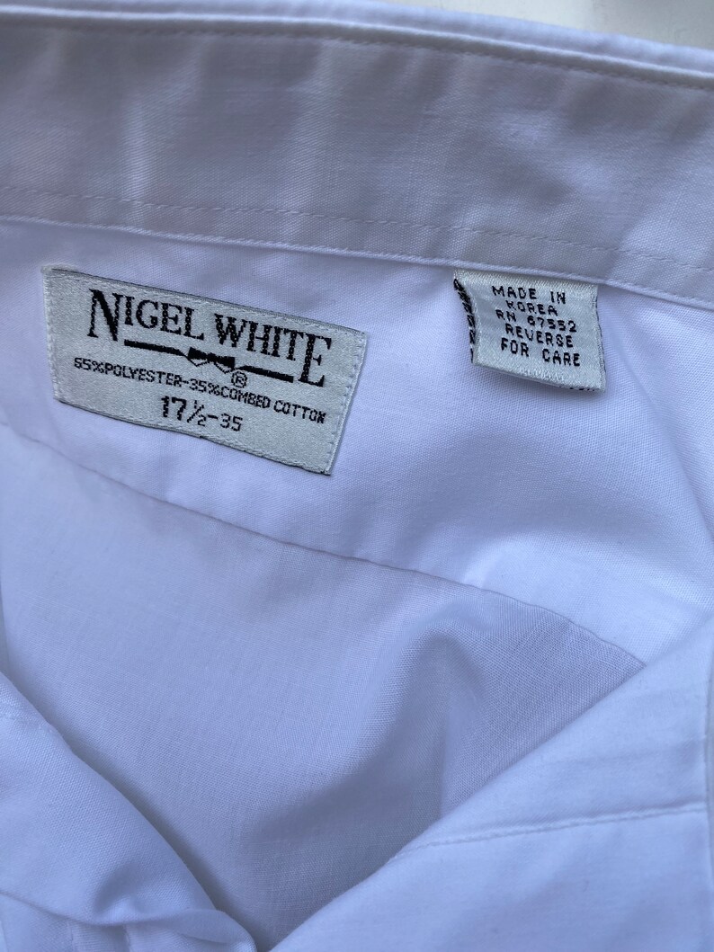 May include: White dress shirt with a label that reads "Nigel White" and "55% Polyester-35% Combed Cotton" and "17 1/2 - 35". The label also has a small bow tie graphic. A second label reads "Made in Korea RN 67552 Reverse for Care".