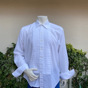 May include: A white long-sleeve dress shirt with a pleated front and French cuffs. The shirt is on a mannequin.