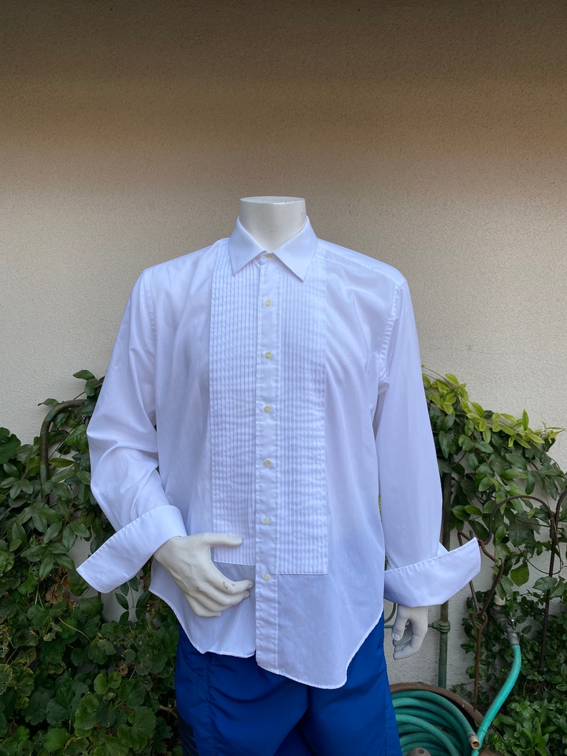 May include: A white long-sleeve dress shirt with a pleated front and French cuffs. The shirt is on a mannequin.