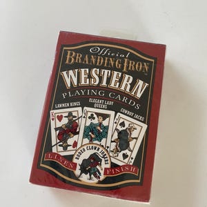 May include: A deck of "Official Branding Iron Western Playing Cards" in a red box. The box features illustrations of playing cards with cowboys and cowgirls. The text on the box includes "Lawmen Kings", "Elegant Lady Queens", and "Cowboy Jacks".