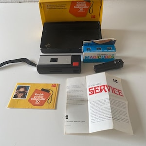 May include: A vintage Kodak Pocket Instamatic 20 camera kit. The kit includes a yellow box, black case, camera, flash, film, and a service manual. The camera is silver and black with a red button. The box reads "Kodak Pocket Instamatic 20".