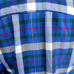 May include: Blue, white, green, and red plaid fabric. The fabric has a woven texture.
