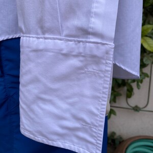 May include: White long-sleeved shirt with a button-down collar and a single button cuff. The shirt is folded and the cuff is visible.