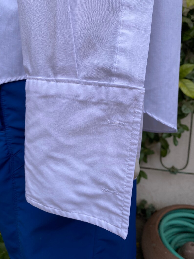 May include: White long-sleeved shirt with a button-down collar and a single button cuff. The shirt is folded and the cuff is visible.