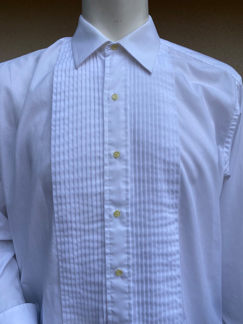 May include: A white dress shirt with a pleated front and a button-down collar.