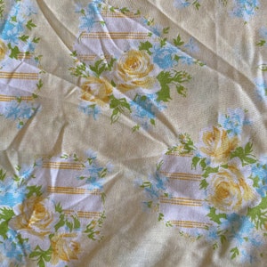 May include: A cream-colored fabric with a repeating pattern of yellow roses and blue flowers. The fabric has a subtle striped pattern.