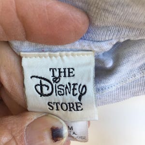 May include: White tag with black text that reads "The Disney Store" on a light blue shirt.
