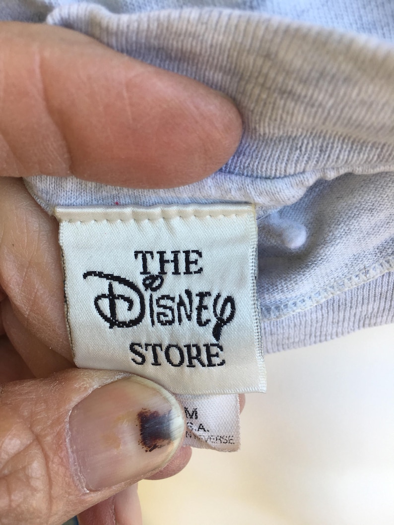 May include: White tag with black text that reads "The Disney Store" on a light blue shirt.