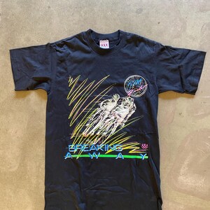 May include: Black t-shirt with a graphic of cyclists racing. The graphic is in neon colors and includes the text "BREAKING AWAY" and "TEAM USA".