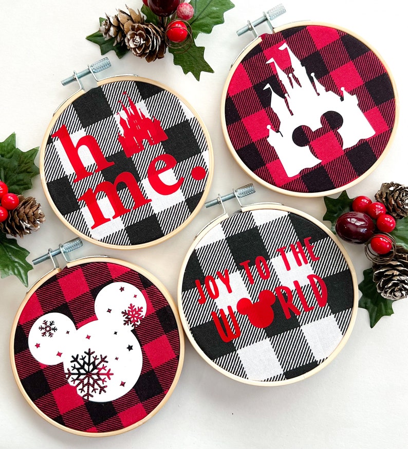 May include: Four round embroidery hoops with red, black, and white buffalo plaid fabric. Each hoop features a different design: a castle, Mickey Mouse, a snowflake, and the words "home" and "Joy to the World" in red.