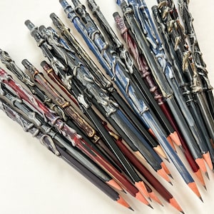May include: A collection of black, red, blue, and gold pencils with intricate, textured designs. The pencils have a variety of finishes, including metallic, glitter, and textured paint.