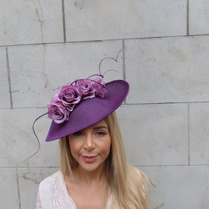 May include: A purple hat with a wide brim and a cluster of pink fabric roses on top. The hat is tilted slightly to the side.