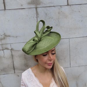 May include: A light green, wide-brimmed hat with a decorative bow. The hat is made of a woven material and has a slightly textured appearance. The hat is a stylish accessory, suitable for special occasions.