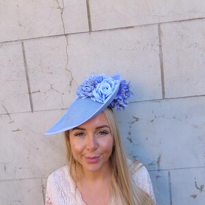 May include: A light blue hat with a wide brim, adorned with a cluster of blue fabric flowers. The hat is a stylish accessory, perfect for special occasions or events.