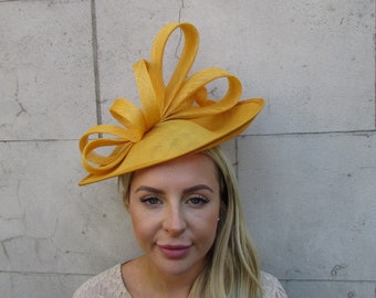 May include: A yellow hat with a large bow on top. The hat is made of straw and has a wide brim. The hat is worn by a person with long blonde hair.