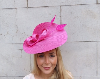 May include: A bright pink hat with a large brim and a bow. The hat has two feathers on the side.
