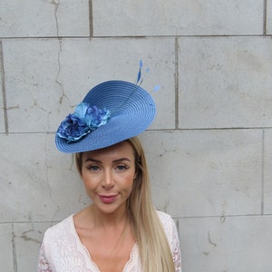 May include: A blue and white hat with a flower accent. The hat is made of straw and has a wide brim. The flower is made of fabric and is in the center of the hat.