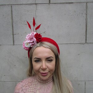 Könnte beinhalten: Ein rotes Stirnband mit einem pinkfarbenen und roten Blumenarrangement und roten Federn. Das Stirnband wird von einer Person mit langen blonden Haaren getragen.