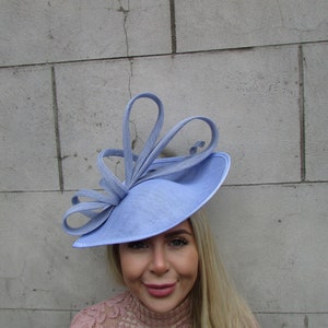 May include: A light blue hat with a large, curled bow. The hat is made of a soft, textured fabric and has a wide brim.