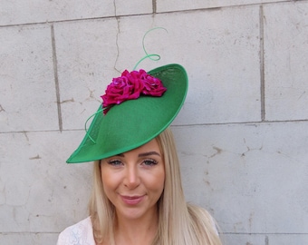 May include: A green hat with a pink flower accent. The hat is tilted at an angle and has a wide brim.