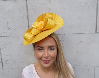 May include: A yellow straw hat with a large yellow flower accent. The hat is worn on the head of a person with long blonde hair.