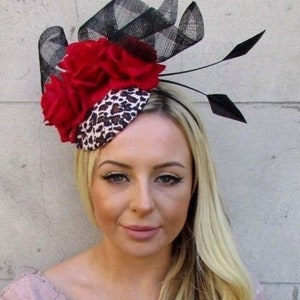 May include: A black and red fascinator with a leopard print base and a black feather accent. The fascinator is adorned with red fabric roses.