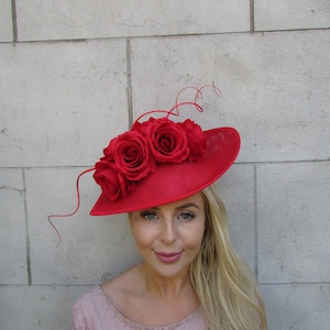 Puede incluir: Un sombrero rojo con una gran rosa roja en la parte superior. El sombrero está hecho de un material suave y de tela y tiene un ala ancha. La rosa está hecha de tela y tiene un aspecto realista.