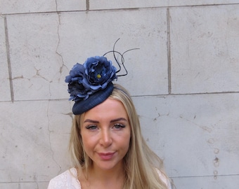 Könnte beinhalten: Ein marineblauer Fascinator mit dunkelblauen Stoffblumen und schwarzen Akzenten. Der Kopfschmuck sitzt auf einer kleinen, runden Basis, perfekt für besondere Anlässe.