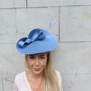 May include: A light blue hat with a large bow and feathers. The hat is made of straw and has a wide brim.