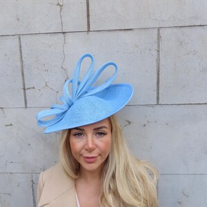 May include: A light blue hat with a large bow on top. The hat is made of a straw-like material and has a wide brim.