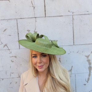 May include: A light green, wide-brimmed hat with a decorative bow. The hat is made of a woven material and has a round crown. The hat is a stylish accessory, perfect for special occasions.