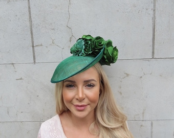 May include: A green fascinator hat with a large green flower on top. The hat is made of a woven material and has a wide brim.