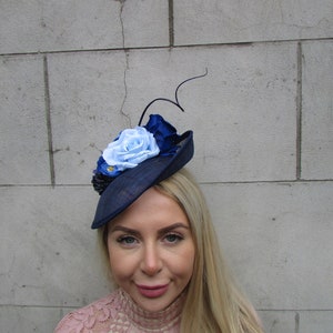 May include: A navy blue hat with a blue and white flower embellishment. The hat is made of a straw-like material and has a wide brim.