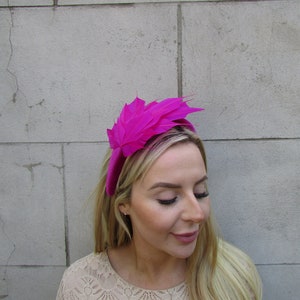 May include: A bright pink headband with a large feather accent. The headband is made of velvet and the feather is made of a soft, fluffy material.